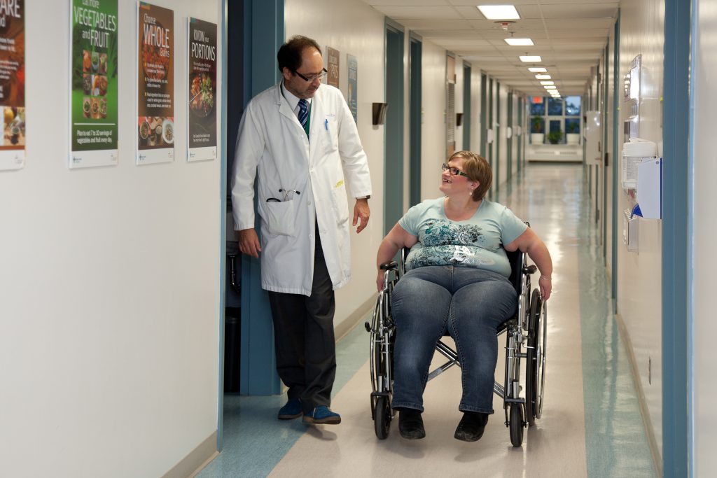 Woman in wheelchair talking to medical professional in hallway