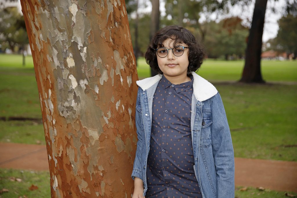 Young boy in park leaning on a tree