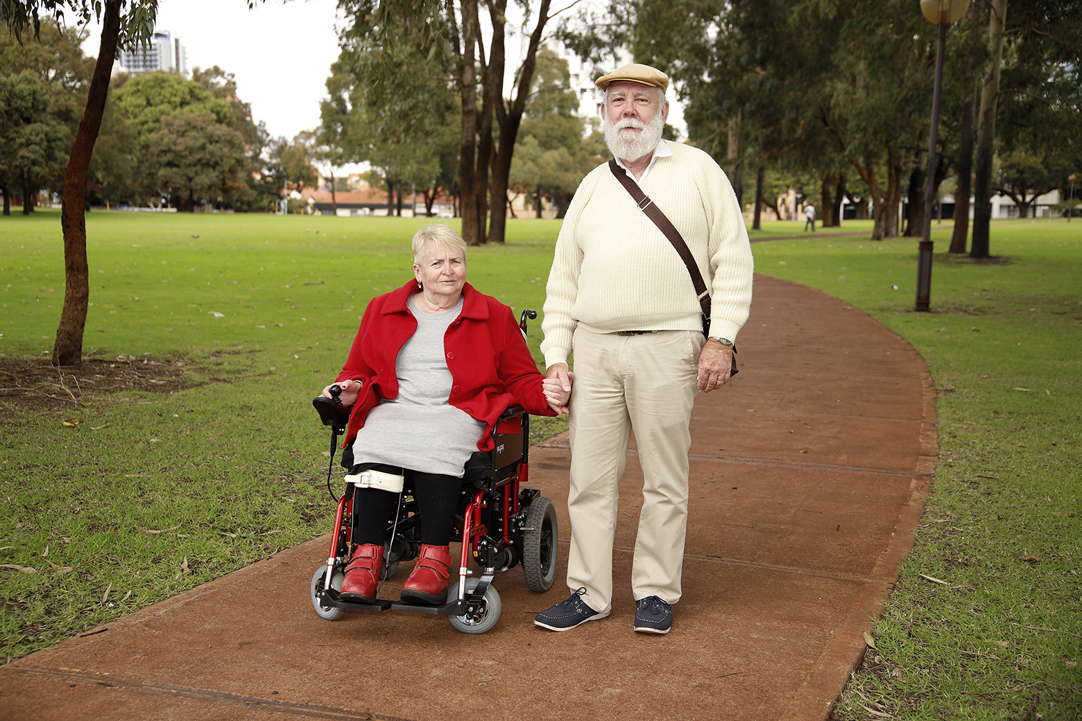 Older woman in wheelchair holder hands with older man walking beside her